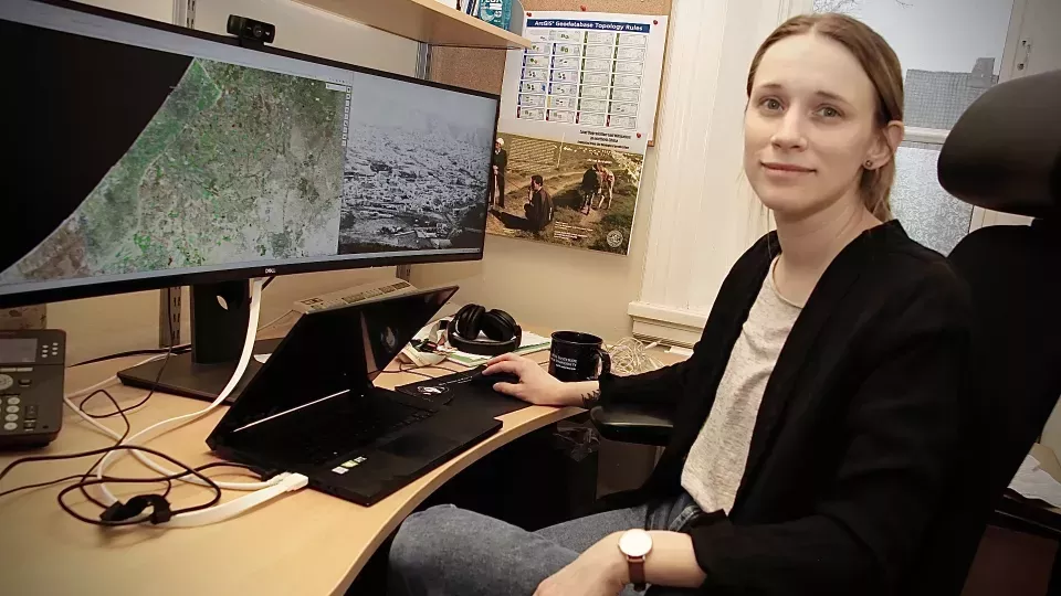 Lina Eklund sitting at her desk in front of a computer with satellite images.