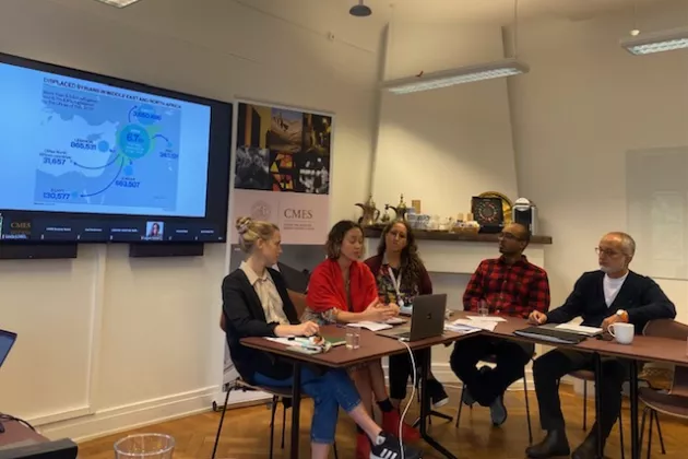 Lina Eklund, Pinar Dinc, Maria Andrea Nardi, Hakim Abdi and Mo Hamza sitting around a table in front of a screen showing a powerpoint presentation.