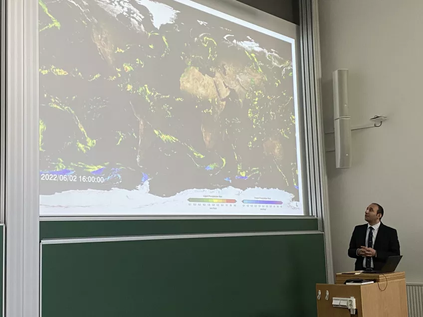 A photo of Hasan at his viva, standing next to a satellite picture of rainfall on Earth